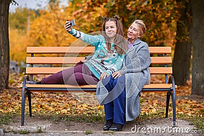 Granddaughter and grandmother do selfie on a bench in an autumn park Stock Photo