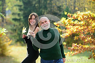 Granddaughter with elderly grandfather standing outdoors in autumn park. Caring adult daughter spend time with old dad. Stock Photo