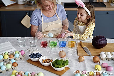 Granddaughter with grandmother dyeing Easter eggs on the table Stock Photo