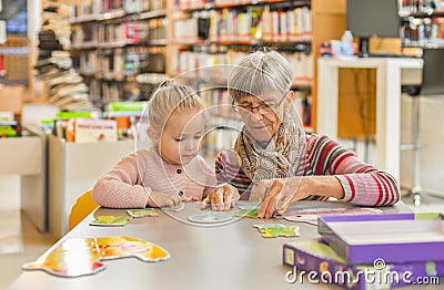 Granddaughter and grandmother put together a puzzle in the library Stock Photo