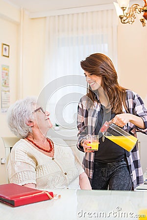 Granddaughter pouring fresh orange juice to her grandmother. Family care concept. Stock Photo