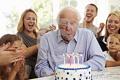 Grandfather Blows Out Birthday Cake Candles At Family Party Stock Photo