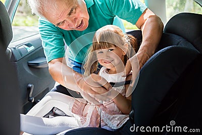 Grandfather Buckling Up On Granddaughter In Car Safety Seat Stock Photo
