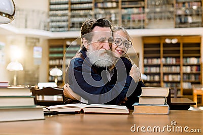 Grandfather and granddaughter or senoir teacher and pupil student, sitting at the table and hugging each other, in old Stock Photo