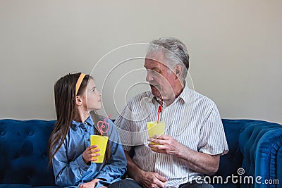 Grandfather and granddaughter sit on the sofa and drink Stock Photo