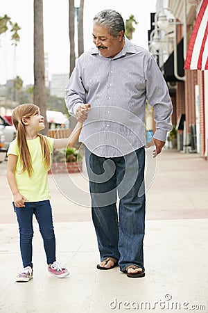 Grandfather With Granddaughter Walking Along Street Stock Photo