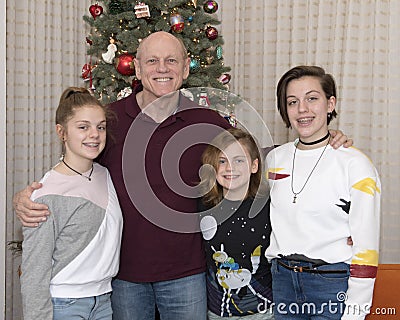 Grandfather and 3 granddaughters standing in front of a Christmas tree Stock Photo