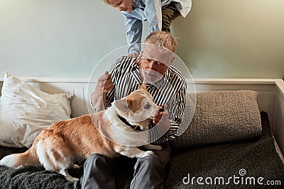 Grandfather and grandson with dog sitting at couch in room Stock Photo