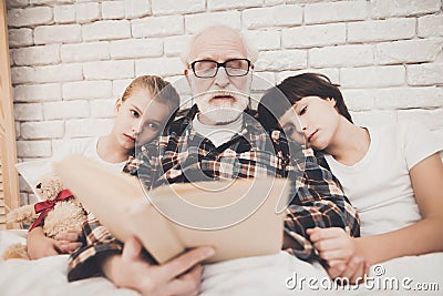 Grandfather, grandson and granddaughter at home. Grandpa and children are reading book. Stock Photo