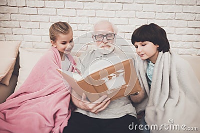 Grandfather, grandson and granddaughter at home. Grandpa and children are watching photos in album. Stock Photo