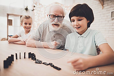 Grandfather, grandson and granddaughter at home. Grandpa and children are playing with dominoes. Stock Photo