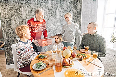 Grandfather holding a red gift and talking his wishes to adorable little girl Stock Photo