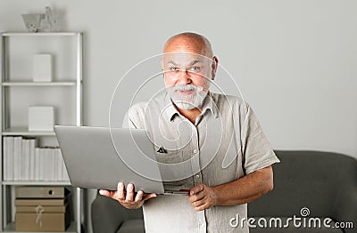 Grandfather, portrait of senior man with a laptop. Senior man with a gray beard at home. Mature man using computer. Stock Photo