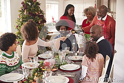 Grandfather pouring champagne at the dinner table during a multi generation, mixed race family Christmas celebration Stock Photo