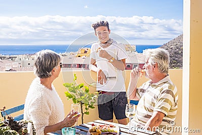 Grandfathers adult mature and teenager nephew enjoy outdoor in the terrace some leisure with food and drinks. ocean and city view Stock Photo