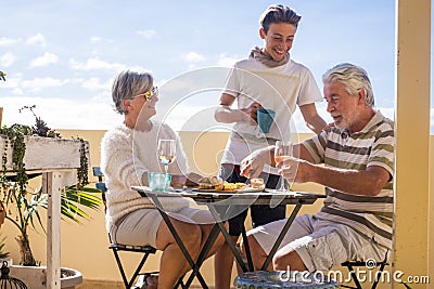 Grandfathers adult mature and teenager nephew enjoy outdoor in the terrace some leisure with food and drinks. ocean and city view Stock Photo