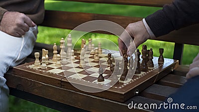 Grandfathers playing chess on bench, moving figures on board, game beginning Stock Photo