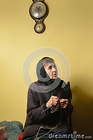 Grandma knitting while looking up aside. Blurry clock above her. Stock Photo