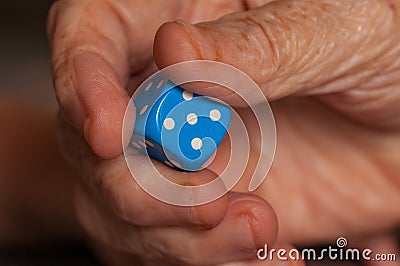 Grandma rolls a blue dice.Social game. Throwing a blue cube Stock Photo