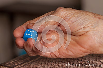 Grandma rolls a blue dice.Social game. Throwing a blue cube Stock Photo