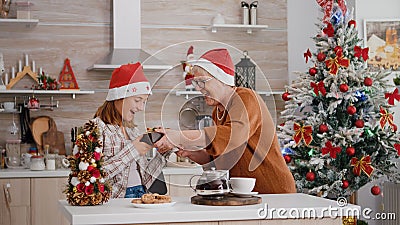 Grandmother bringing wrapper present gift with ribbon on it to granddaughter enjoying christmastime Stock Photo