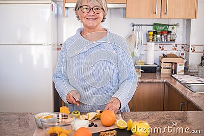 Grandmother with glasses cut fruit and smiling - lifestyle health, healhy - kitchen in the background - cooking at home Stock Photo