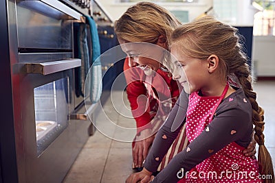 Grandmother And Granddaughter Waiting By Oven In Kitchen At Home For Cakes To Bake Stock Photo