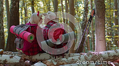 Grandmother grandfather senior tourists hikers sitting on tree and hugging, kissing in summer forest Stock Photo