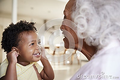 Grandmother Sitting On Sofa At Home With Baby Granddaughter Playing Game Together Stock Photo