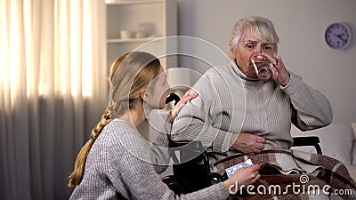 Grandmother taking pill with water, caring granddaughter supporting sick woman Stock Photo