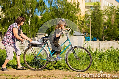 Grandmother teaches little granddaughter to ride bike Stock Photo