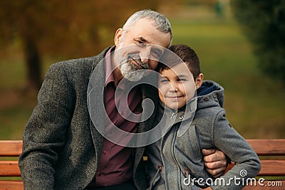 Grandpa and his grandson spend time together in the park. They are sitting on the bench. Walking in the park and Stock Photo