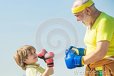 Grandpa and little child boy in boxing stance doing exercises with boxing gloves. Elderly man hitting punching bag Stock Photo