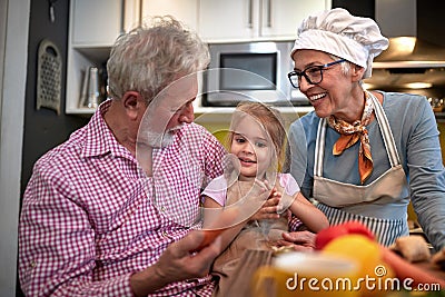 Grandpa persuading his granddaughter to eat carrot. grandma watching and laughing Stock Photo