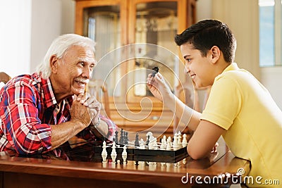 Grandpa Playing Chess Board Game With Grandson At Home Stock Photo
