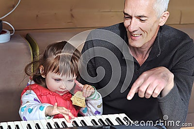 Grandpa teaches little girl to play piano. Concept of music study and creative hobby Stock Photo