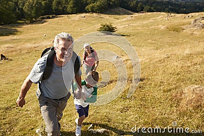 Grandparents With Grandchildren Climbing Hill On Hike Through Countryside In Lake District UK Together Stock Photo