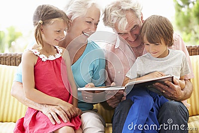 Grandparents And Grandchildren Reading Book On Garden Seat Stock Photo