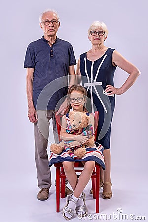 Grandparents and granddaughter on a gray background in full length Stock Photo