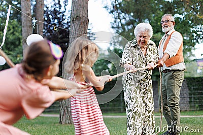 Grandparents have tug of war with their granddaughters. Fun games at family garden party. Stock Photo