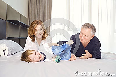 Grandparents play with the grandson of a child in a room. Stock Photo