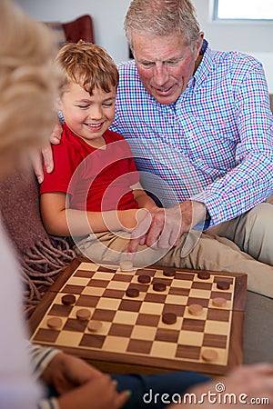 Grandparents Playing Board Game Of Draughts With Grandchildren At Home Stock Photo