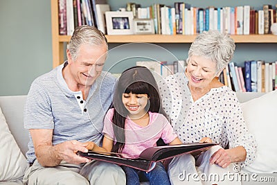 Grandparents showing album to granddaughter at home Stock Photo