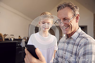 Grandson Showing Grandfather How To Solve Problem And Use Mobile Phone At Home Stock Photo