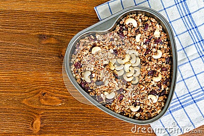 Granola in a heart-shaped baking sheet on a wooden table. Food Concept Stock Photo