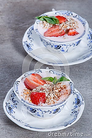 Granola, muesli with strawberries and yogurt decorate with mint in a ceramic bowls on wood grey background Stock Photo