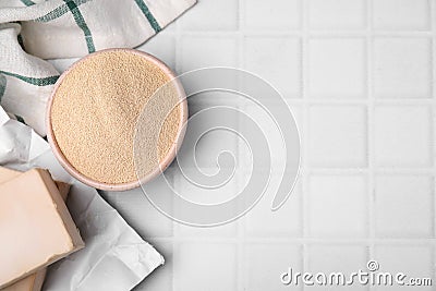 Granulated and compressed yeast in bowl on white tiled table, flat lay. Space for text Stock Photo
