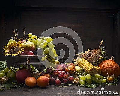 Grape, apples and autumn fruits and vegetables in an iron bowl with a sunflower on a wooden table on a dark wall background Stock Photo