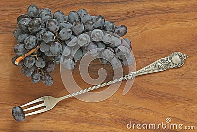 Grapes. A bunch of dark, black grapes lies on a wooden board close-up and a vintage fork Stock Photo