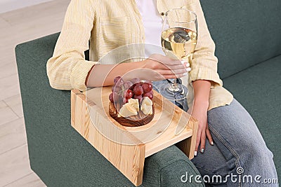 Grapes and cheese on sofa armrest wooden table. Woman holding glass of wine at home, closeup Stock Photo